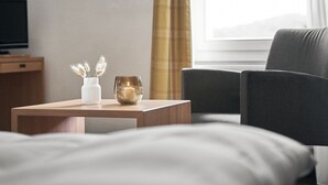 Habitación de hotel con cama, mesita de noche con un florero y una vela, televisión y ventana con cortinas.