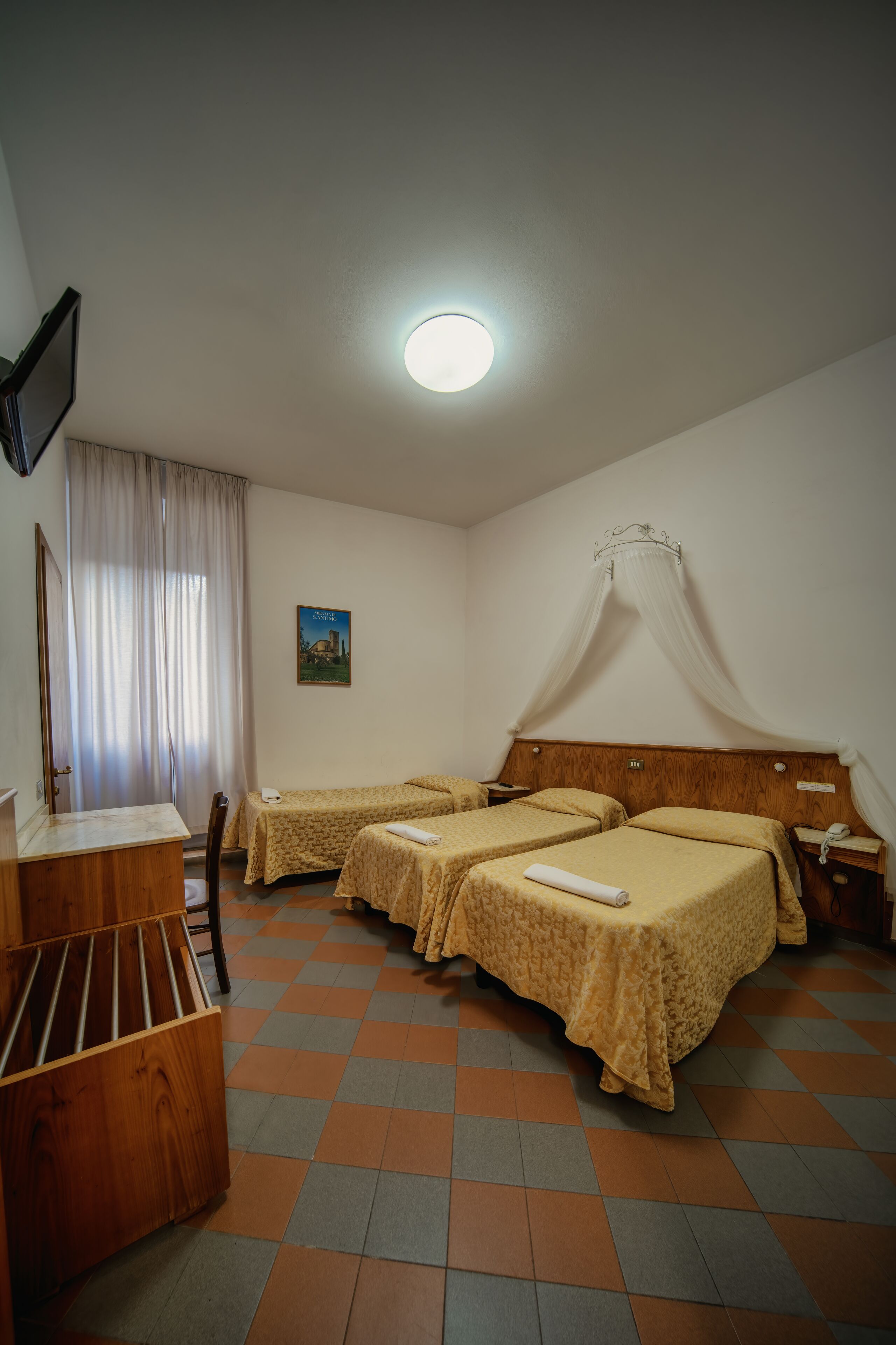 A hotel room with two beds, a desk, a chair, a TV, and a window with curtains.