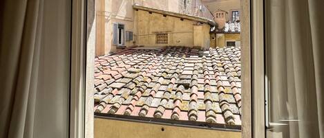 Vista pela janela de um edifício com telhado de telhas e porta com cortinas.