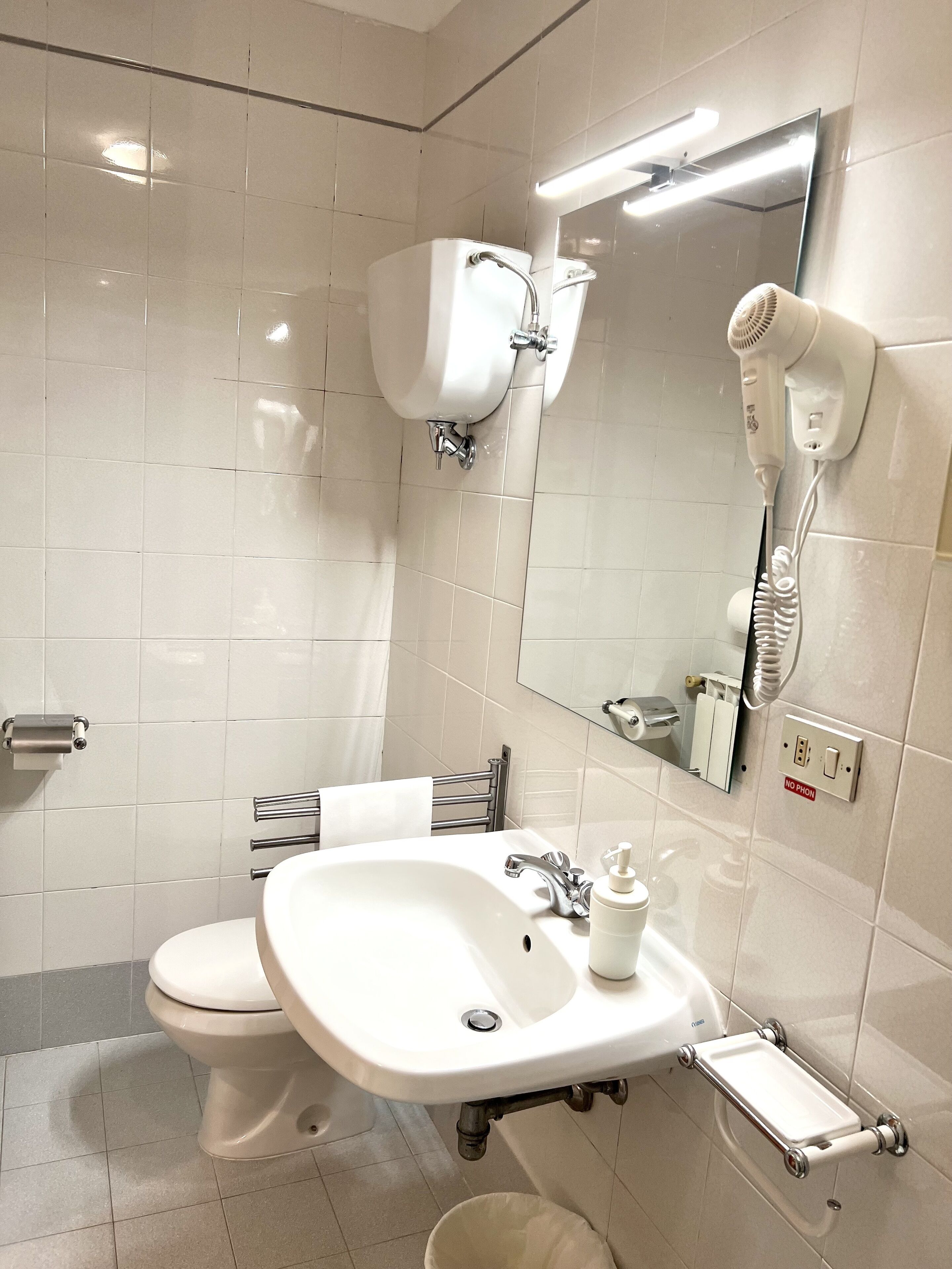 A modern bathroom with a toilet, sink, mirror, and hairdryer.