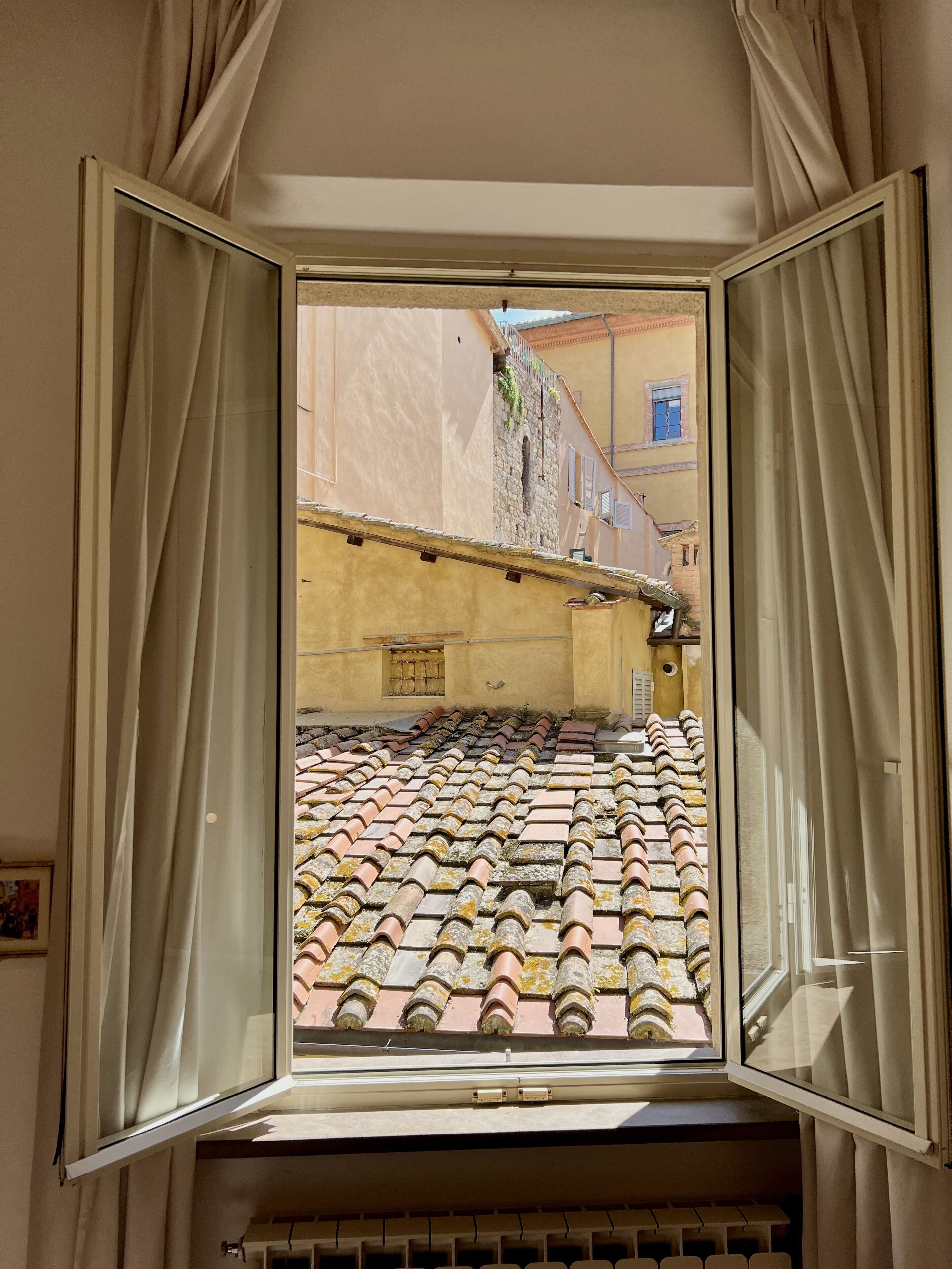 A room with a large window overlooking a tiled roof and a building with a yellow facade.