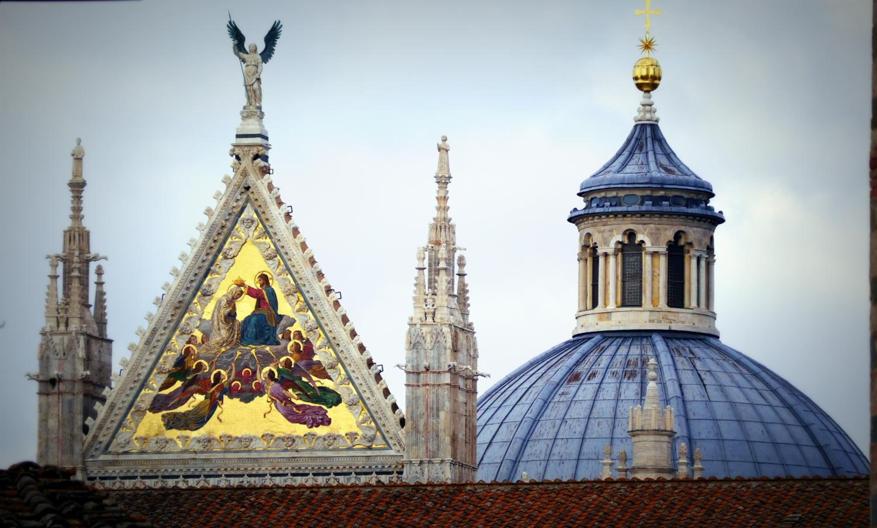 Una chiesa con una grande cupola dorata e un tetto triangolare sormontato da una statua.