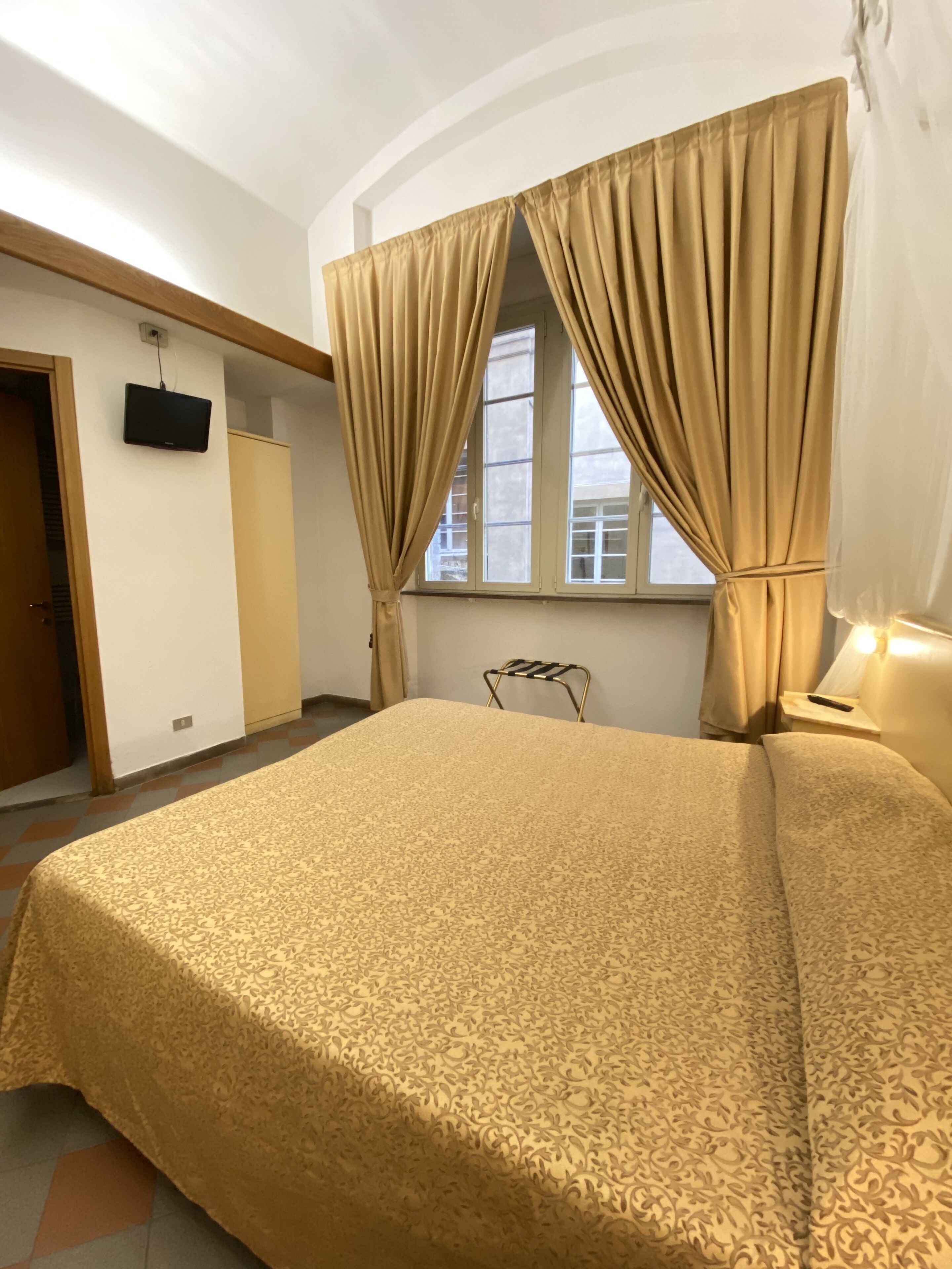 A bedroom with a bed, curtains, a television, and a window.