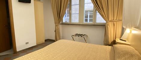 A bedroom with a bed, curtains, a television, and a window.