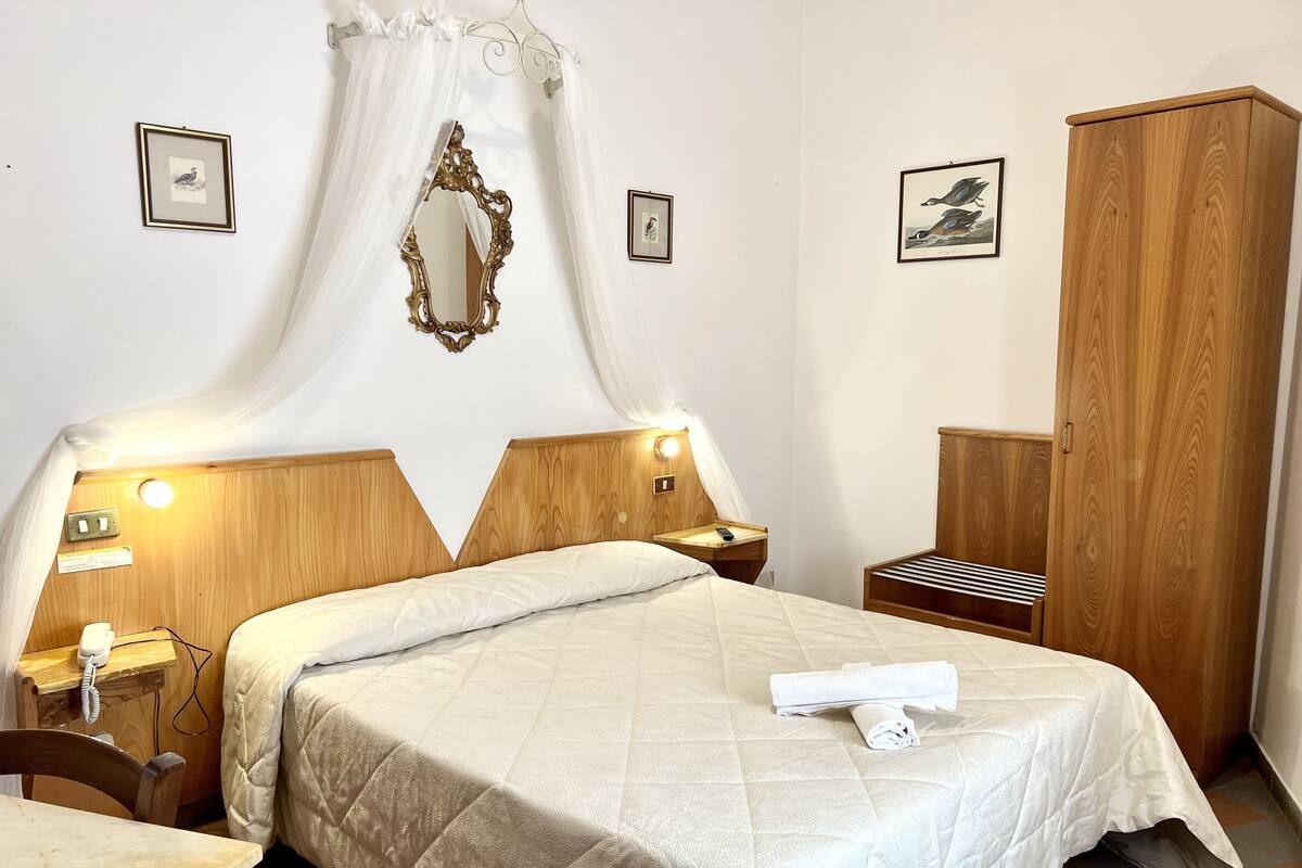A neatly arranged hotel room with a bed, bedside tables, a wardrobe, and a mirror.