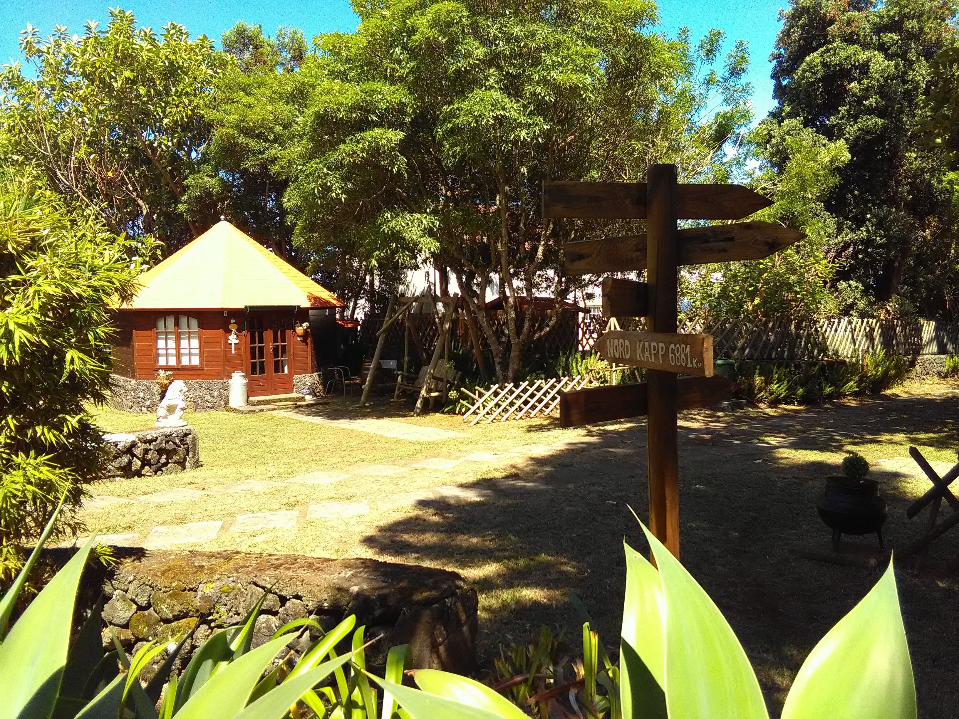 A wooden signpost with directional arrows, a small red building with a yellow roof, and a stone wall in a garden setting.
