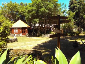 A wooden signpost with directional arrows, a small red building with a yellow roof, and a stone wall in a garden setting. - Vilar dos Carvalhinhos (Praia da Vitoria)