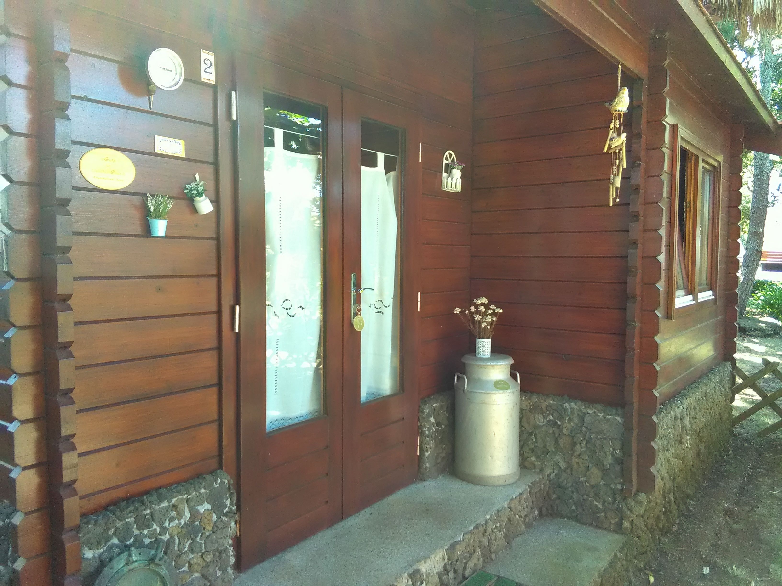 A wooden building with two doors, a small potted plant, and a metal container on the porch.