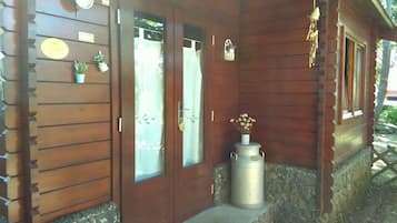 A wooden building with two doors, a small potted plant, and a metal container on the porch.