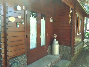 A wooden building with two doors, a small potted plant, and a metal container on the porch. - Vilar dos Carvalhinhos (Praia da Vitoria)