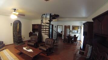 A spacious living room with a fireplace, a dining area, and a staircase leading to an upper level.