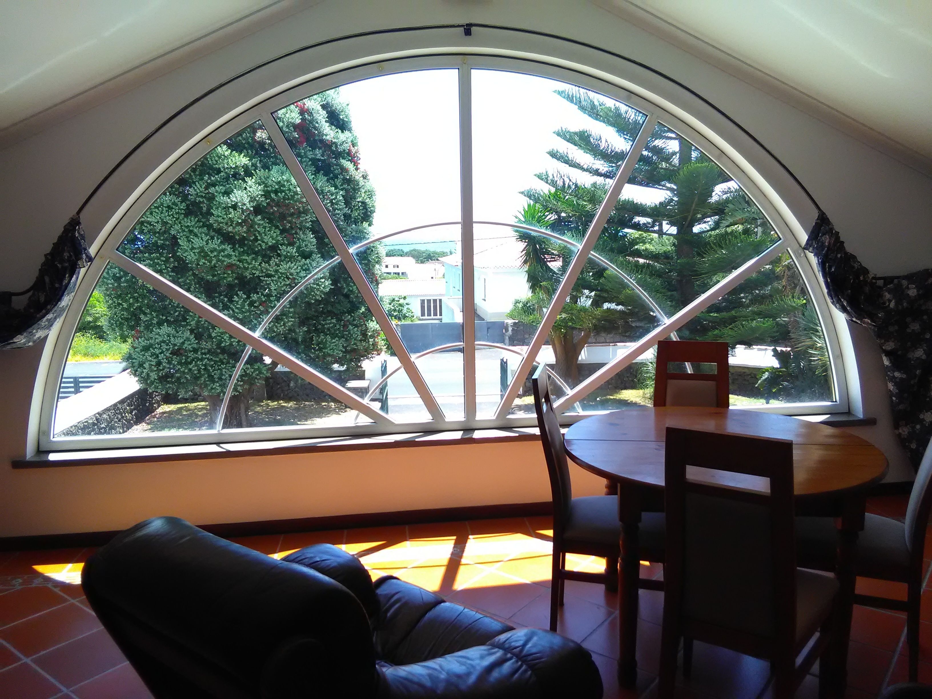 A room with a large arched window, a dining table with chairs, and a leather chair.