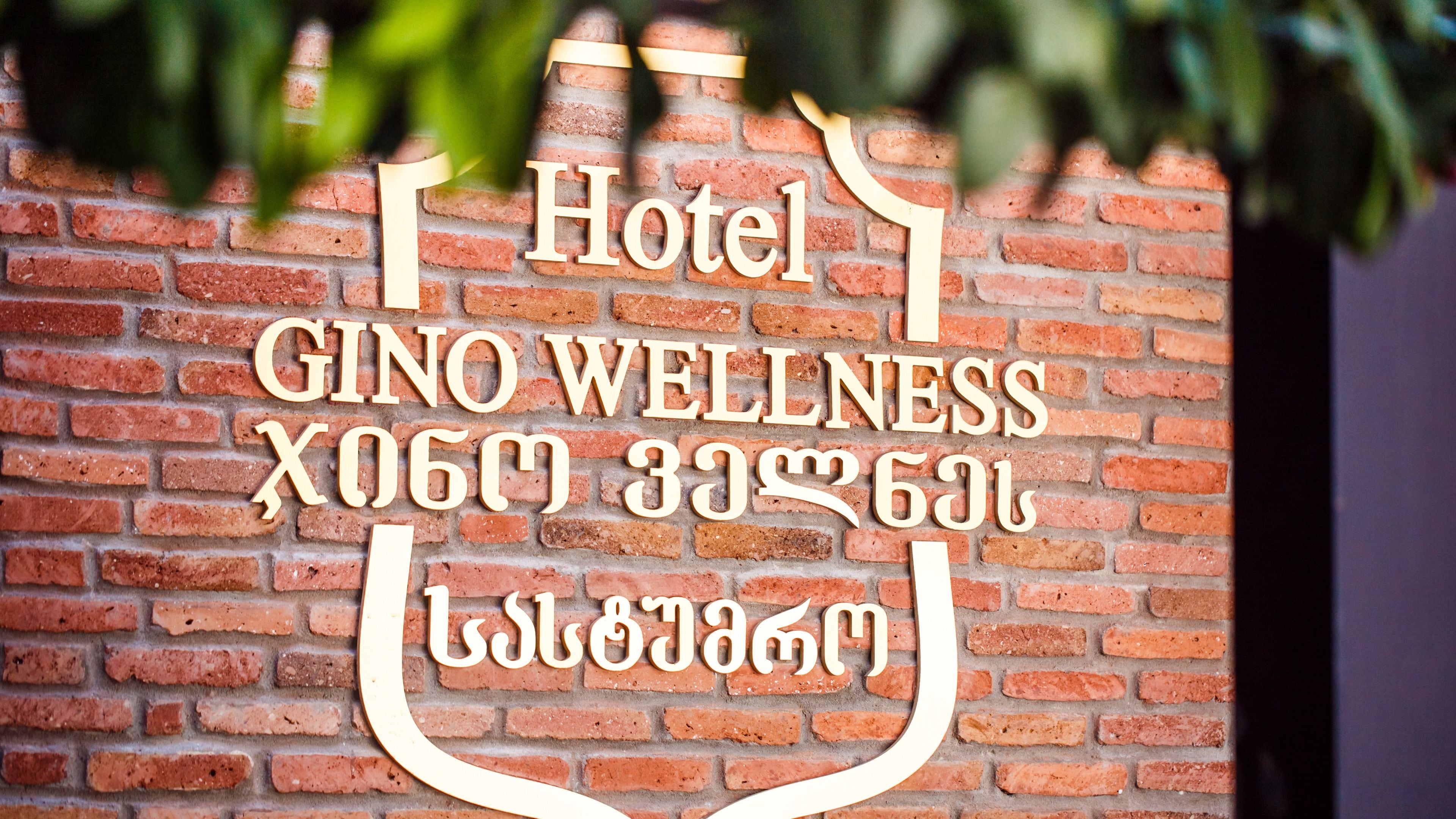 Un muro de ladrillo con un letrero que dice 'Hotel GINO WELLNESS' y algo de texto en otro idioma.