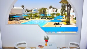 A poolside view with a clear blue pool, white walls, and blue umbrellas. - Zenon Hotel Djerba (Mezraia)