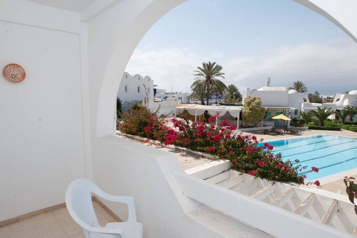 A white interior with a view of a swimming pool, outdoor seating, and a staircase leading to a terrace.