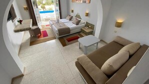 A modern hotel room with a bed, a sofa, a small table, and a view of the pool. - Zenon Hotel Djerba (Mezraia)