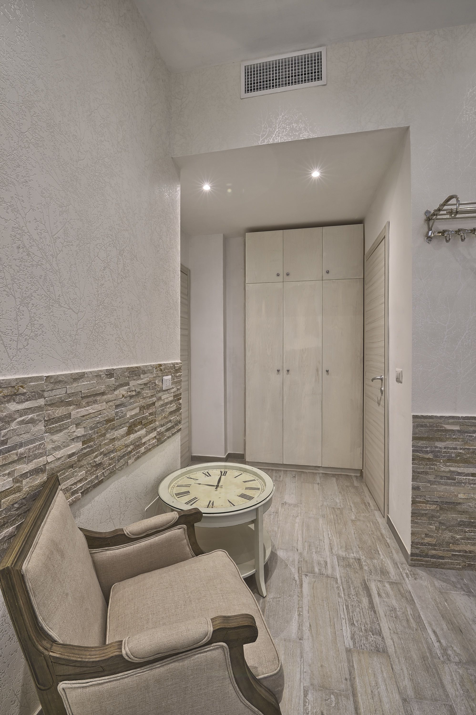 A corner room with a bench, a round table with a clock, and a wardrobe.