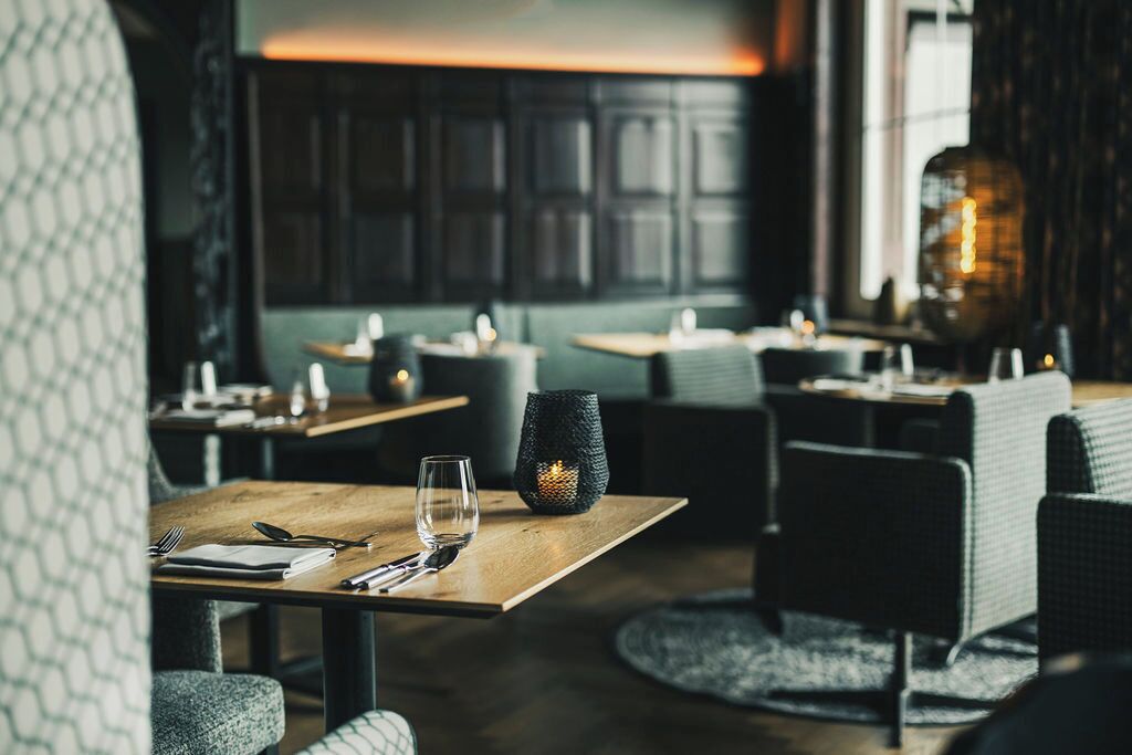 Interior de restaurante con mesas de madera, sillas acolchadas e iluminación cálida.