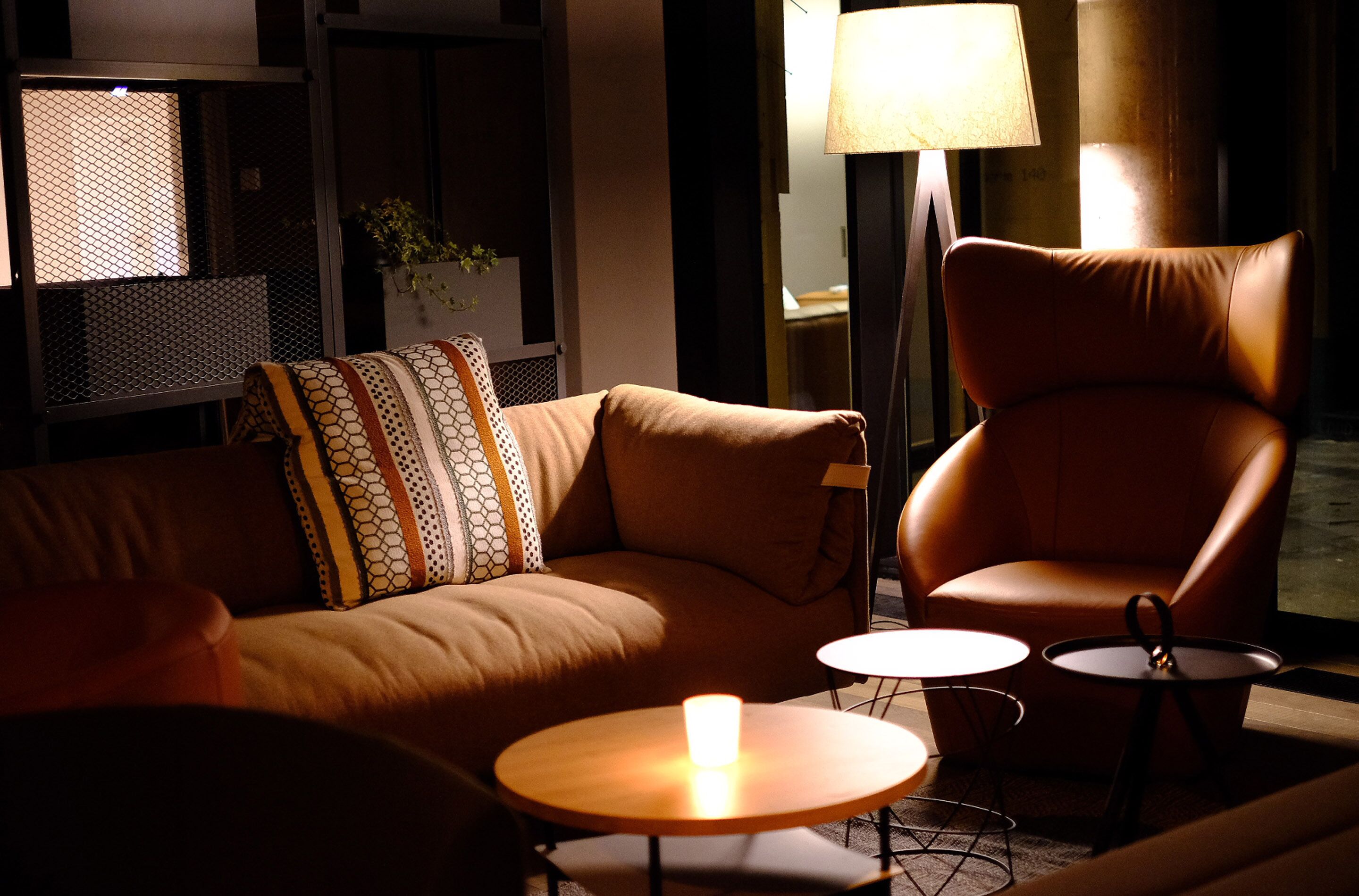 A cozy living room with a brown leather sofa, a brown leather armchair, and two small round tables with candles.