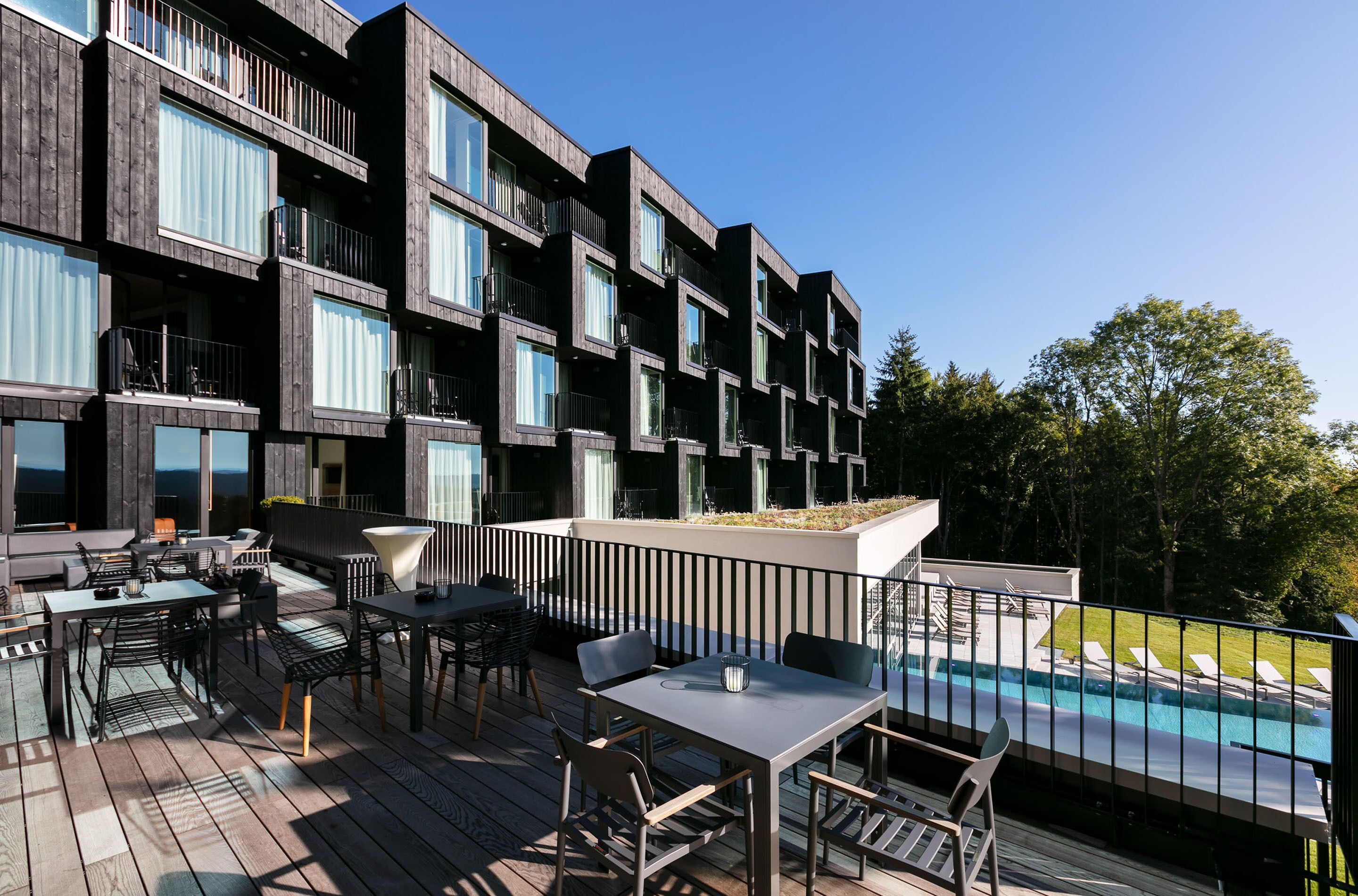 A modern building with balconies, outdoor seating, and a pool.