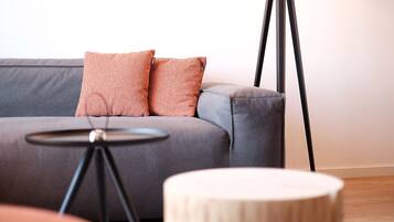 A modern living room with a grey sofa, two pink cushions, a small round wooden table, and a floor lamp.