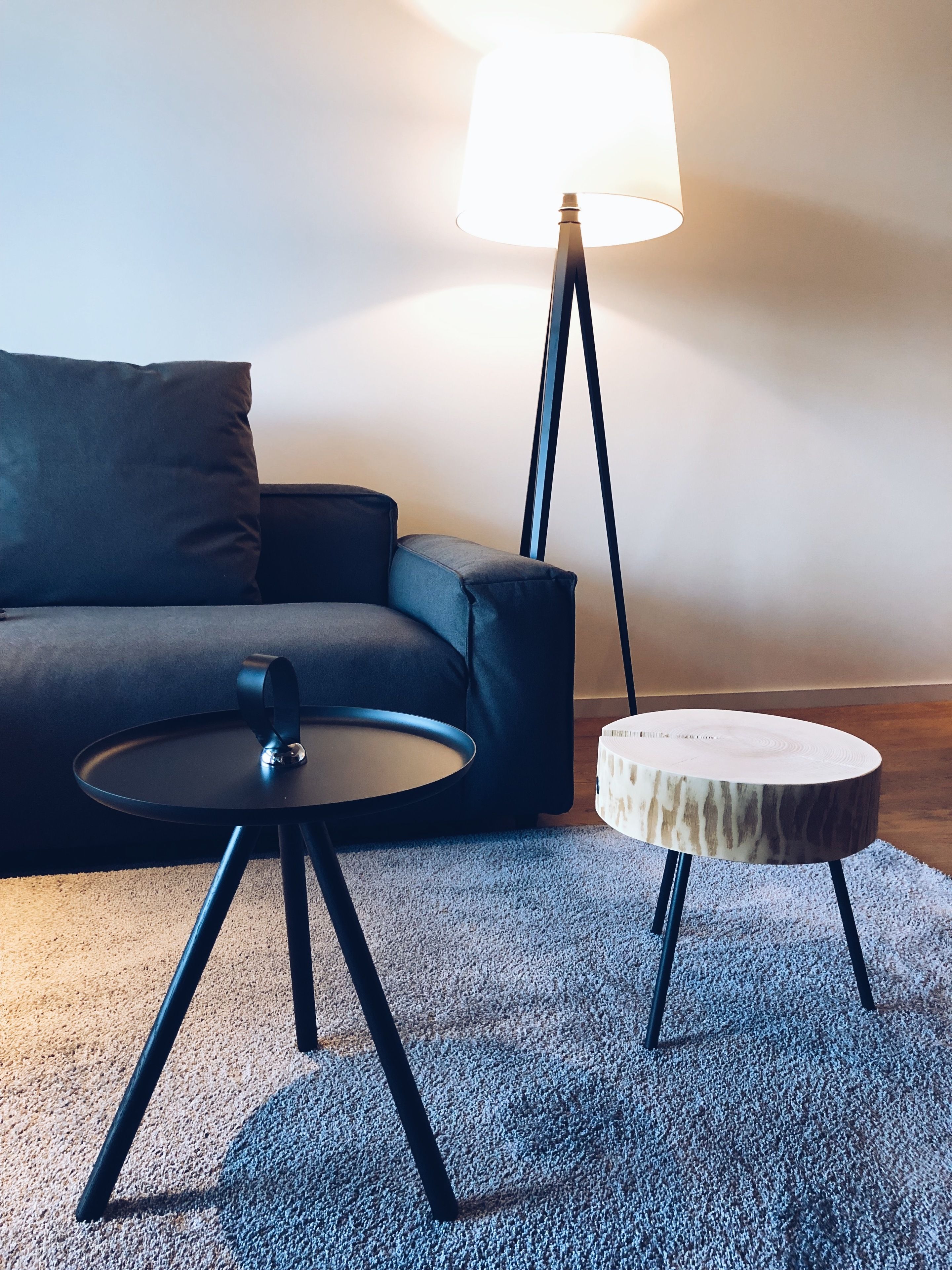 A modern living room with a grey sofa, a round black coffee table, and a small round side table with a natural wood finish.
