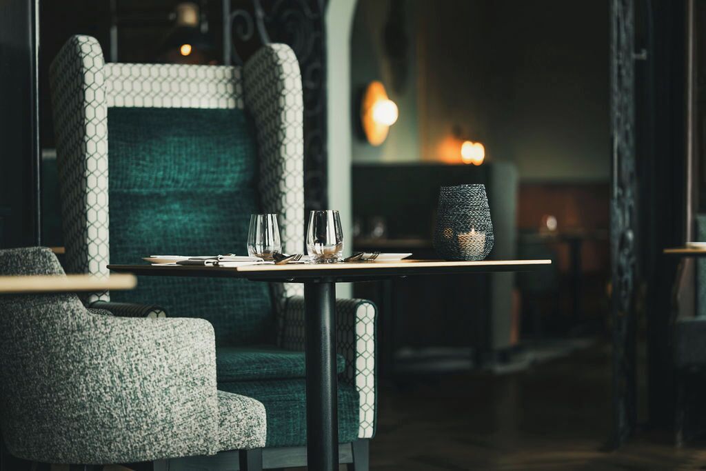 Un comedor con una mesa preparada para dos personas, un sillón estampado y un sofá con textura.