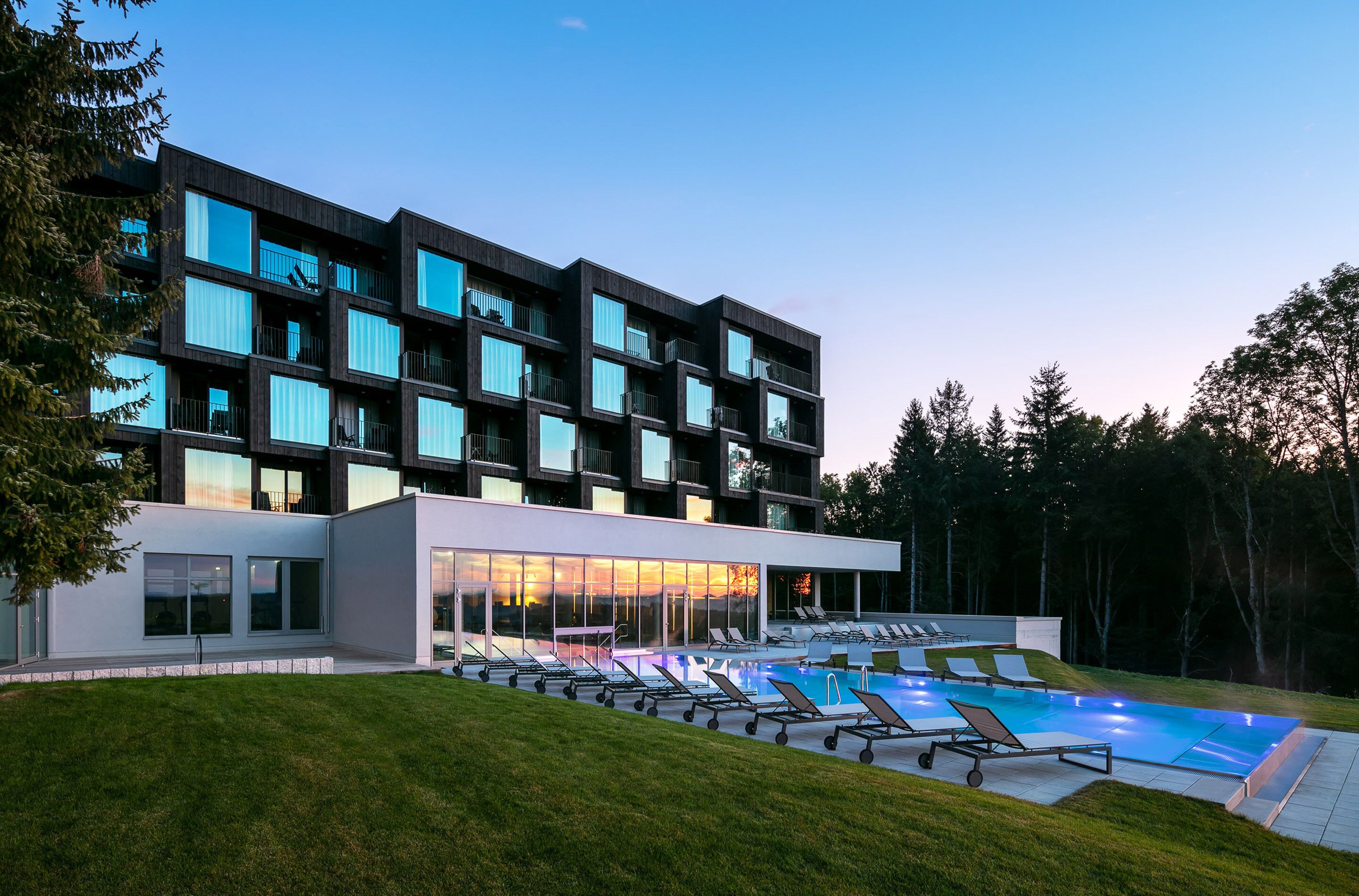 Un hotel moderno con piscina, varios balcones y un césped bien cuidado.
