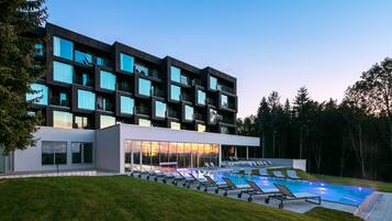 Un hotel moderno con piscina, varios balcones y un césped bien cuidado.