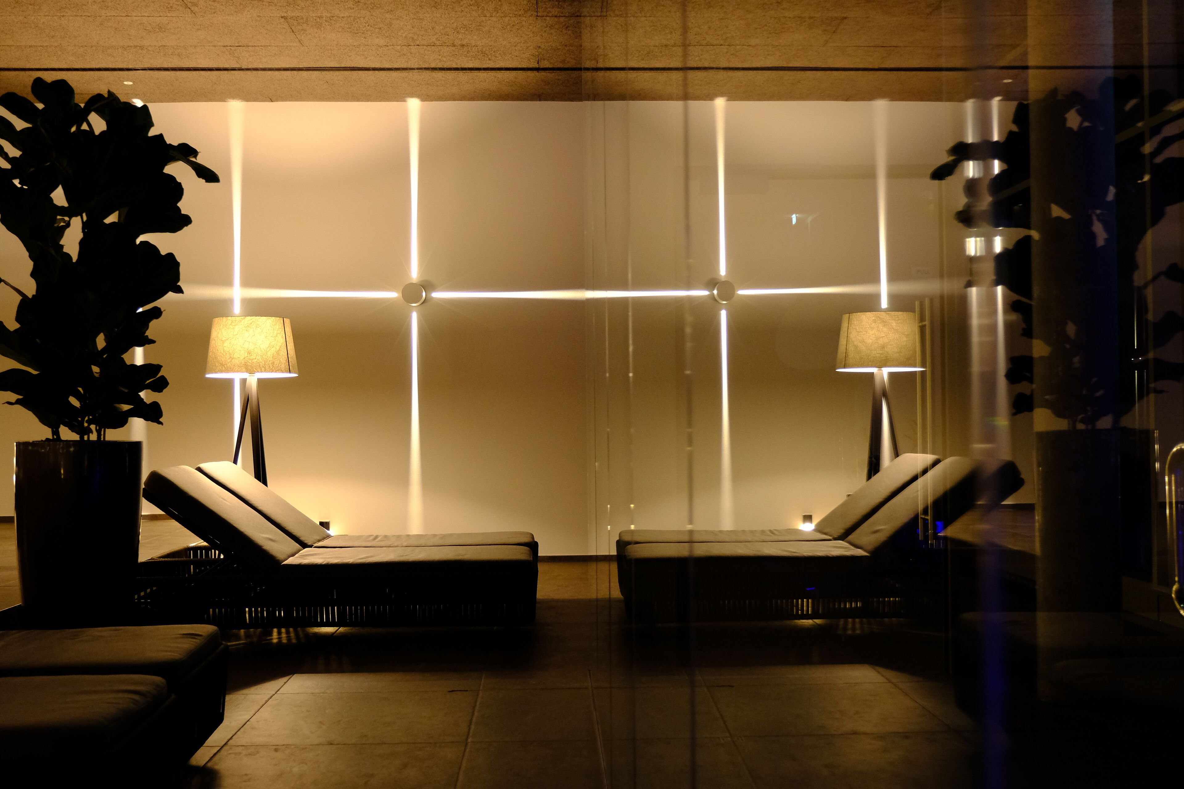 Un área de descanso moderna con dos sillones reclinables, una planta grande en maceta y una pared con líneas iluminadas.