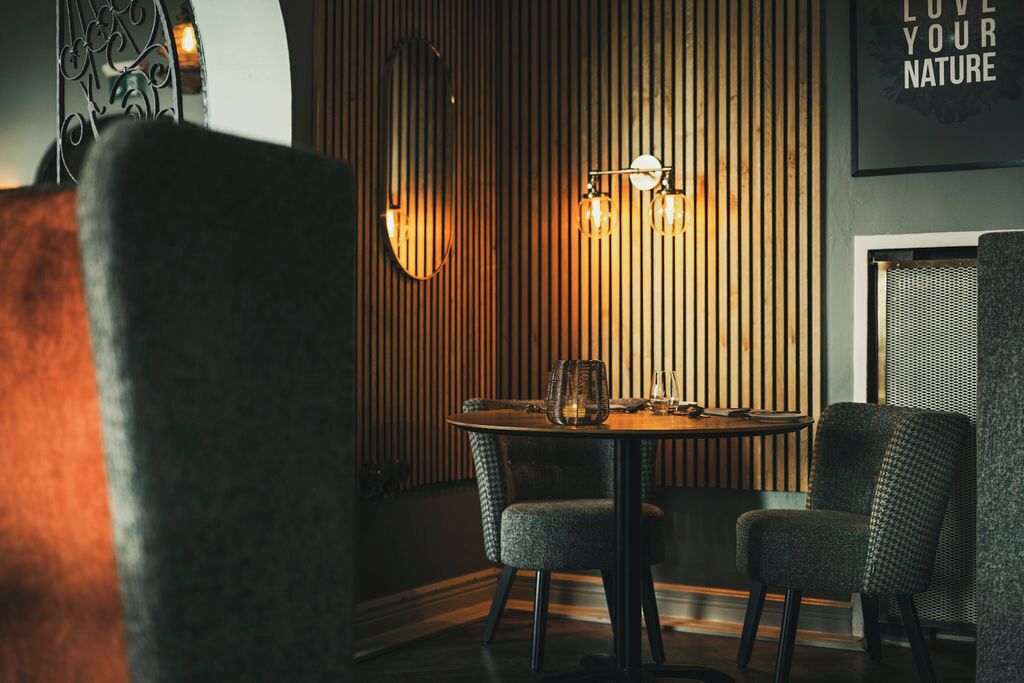 Un coin repas comprenant une table ronde, deux chaises et un mur avec des lambris en bois verticaux.