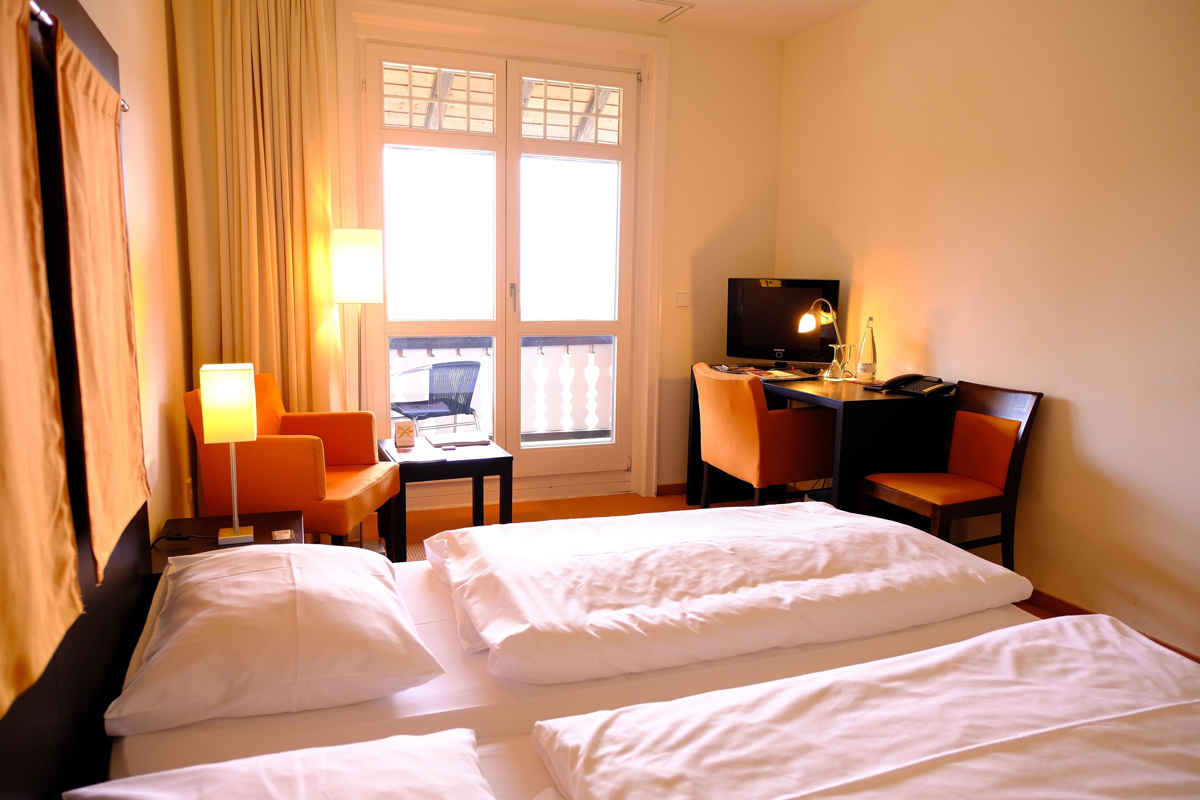 Una habitación de hotel con dos camas, un escritorio con silla, un televisor y una ventana con cortinas.