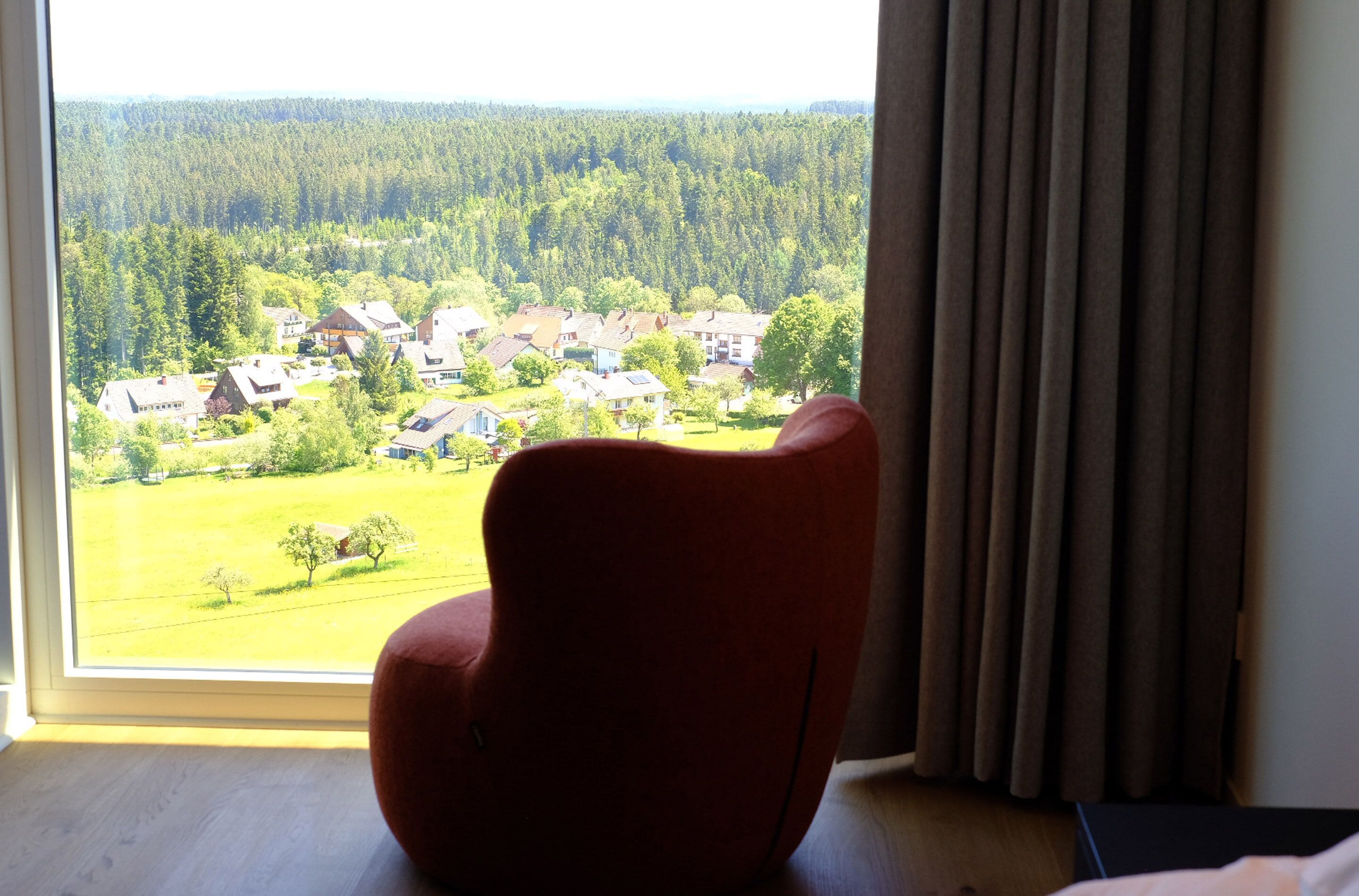 A room with a large window overlooking a residential area and a forest.