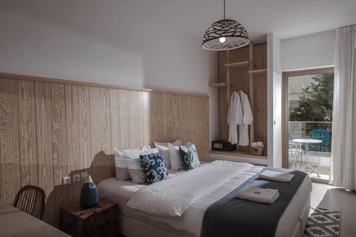 A modern hotel room with a large bed, wooden headboard, and a view of the outdoors through a sliding glass door.