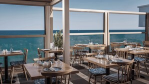 A seaside restaurant with tables and chairs, large windows, and a view of the ocean. - Serenity Spritz Hotel - Adults Only (Hersonissos)