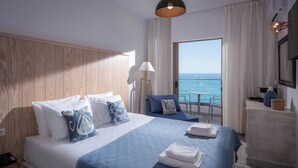 A hotel room with a large bed, a desk, a chair, and a view of the sea. - Serenity Spritz Hotel - Adults Only (Hersonissos)