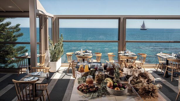 A dining area with tables and chairs, a buffet with fruits and snacks, and a view of the sea with a sailboat. - Serenity Spritz Hotel - Adults Only (Hersonissos)