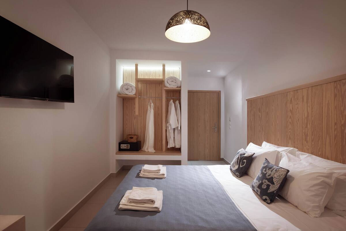 A modern bedroom with a large bed, a TV mounted on the wall, a wooden wardrobe, and a hanging light fixture.