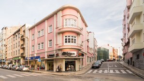 A pink building with a storefront, parked cars, and a pedestrian crossing. - The Bohemian Place (Aveiro)