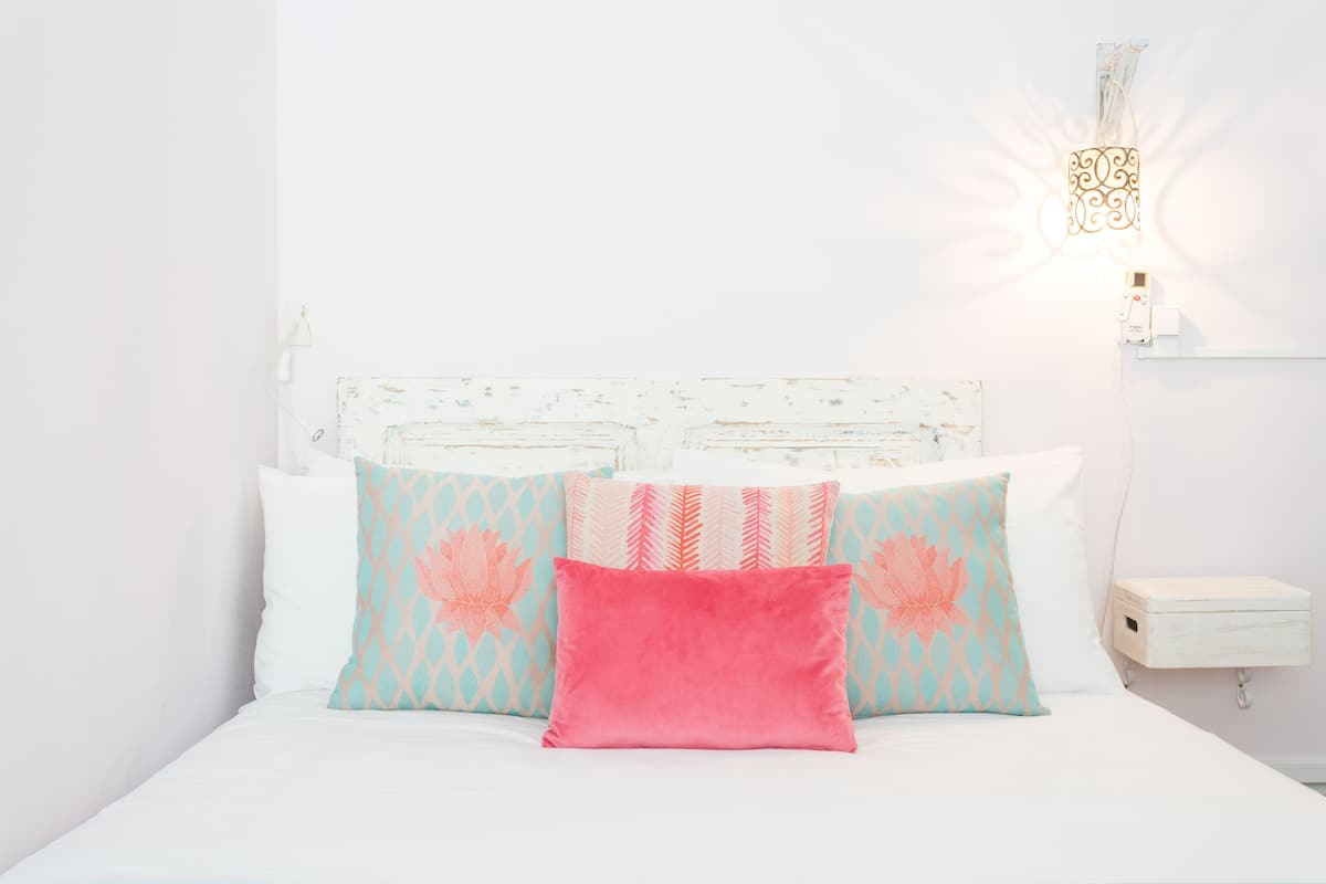 Una cama bien hecha con almohadones estampados y una lámpara de pared.