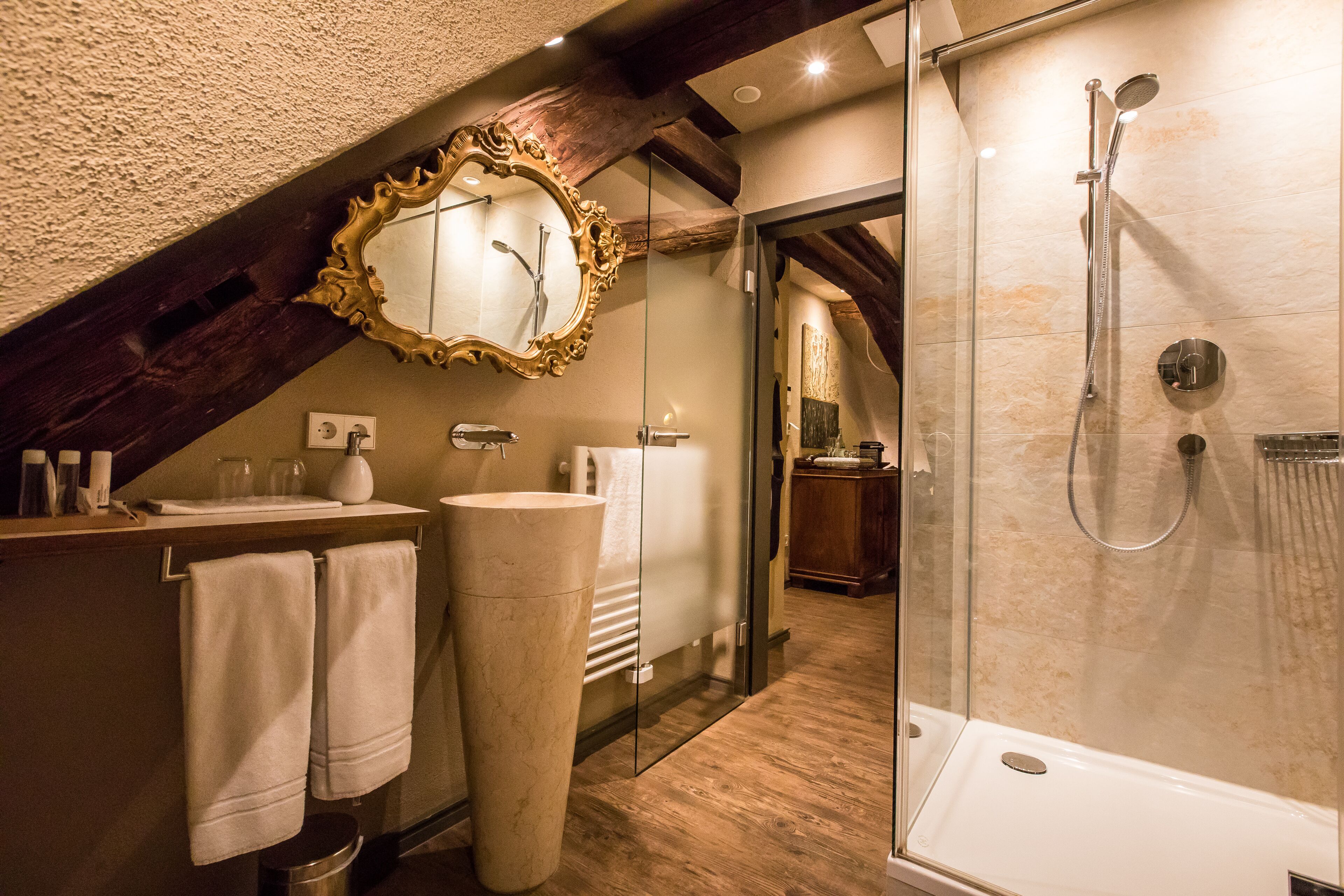 A modern bathroom with a large mirror, a glass-enclosed shower, and a wooden ceiling.