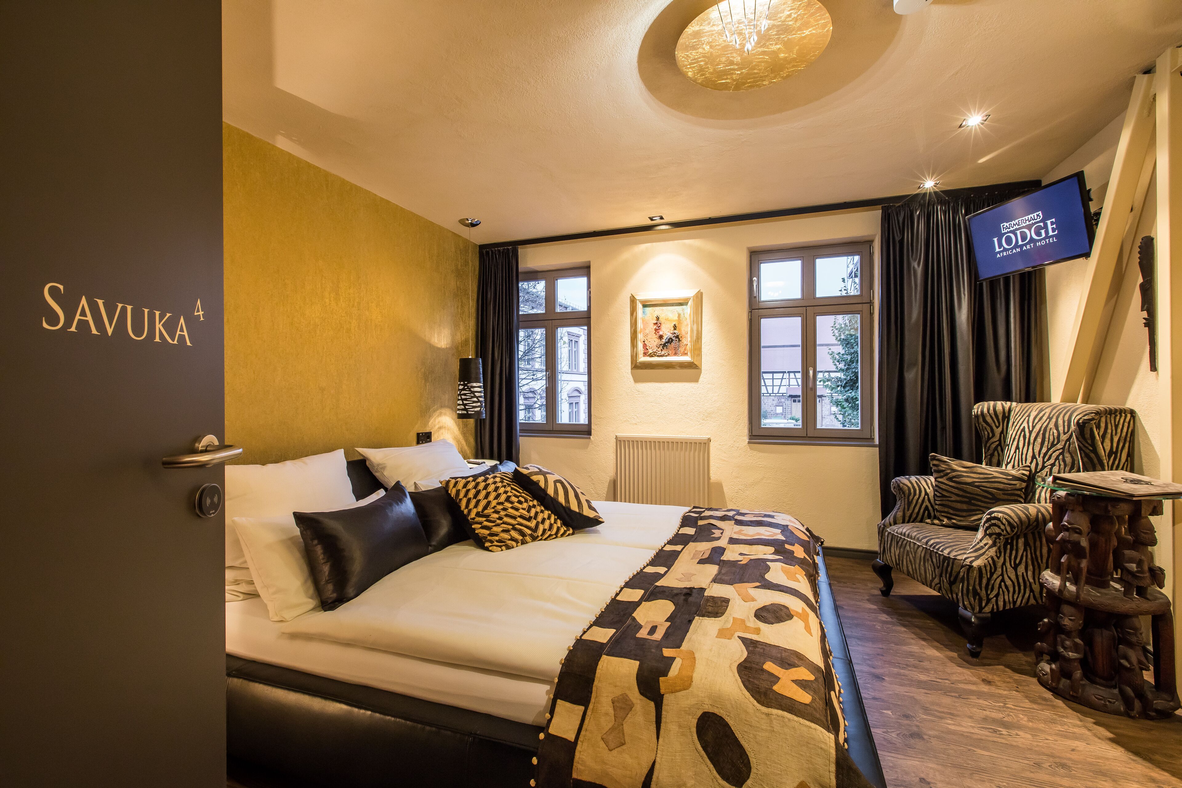 A hotel room with a bed, a zebra-striped armchair, a television, and a large window.