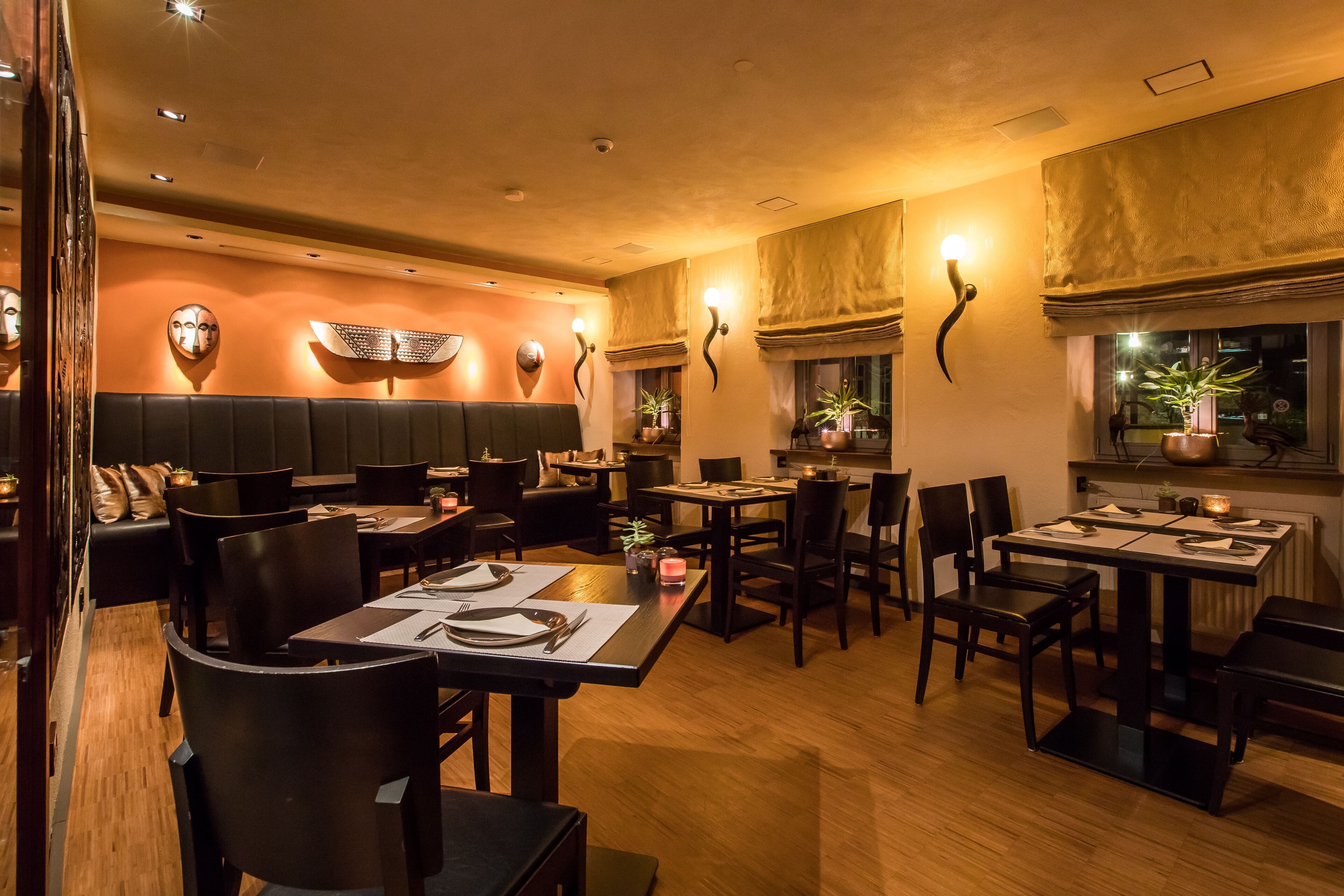 A restaurant with booths, tables, and chairs. There are wall-mounted lights and a window with a plant.