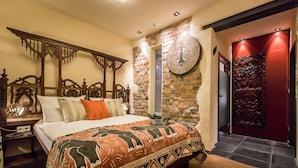 Quarto com uma cama grande, cabeceira de madeira, parede de destaque em pedra, porta vermelha e mesa de cabeceira com abajur.