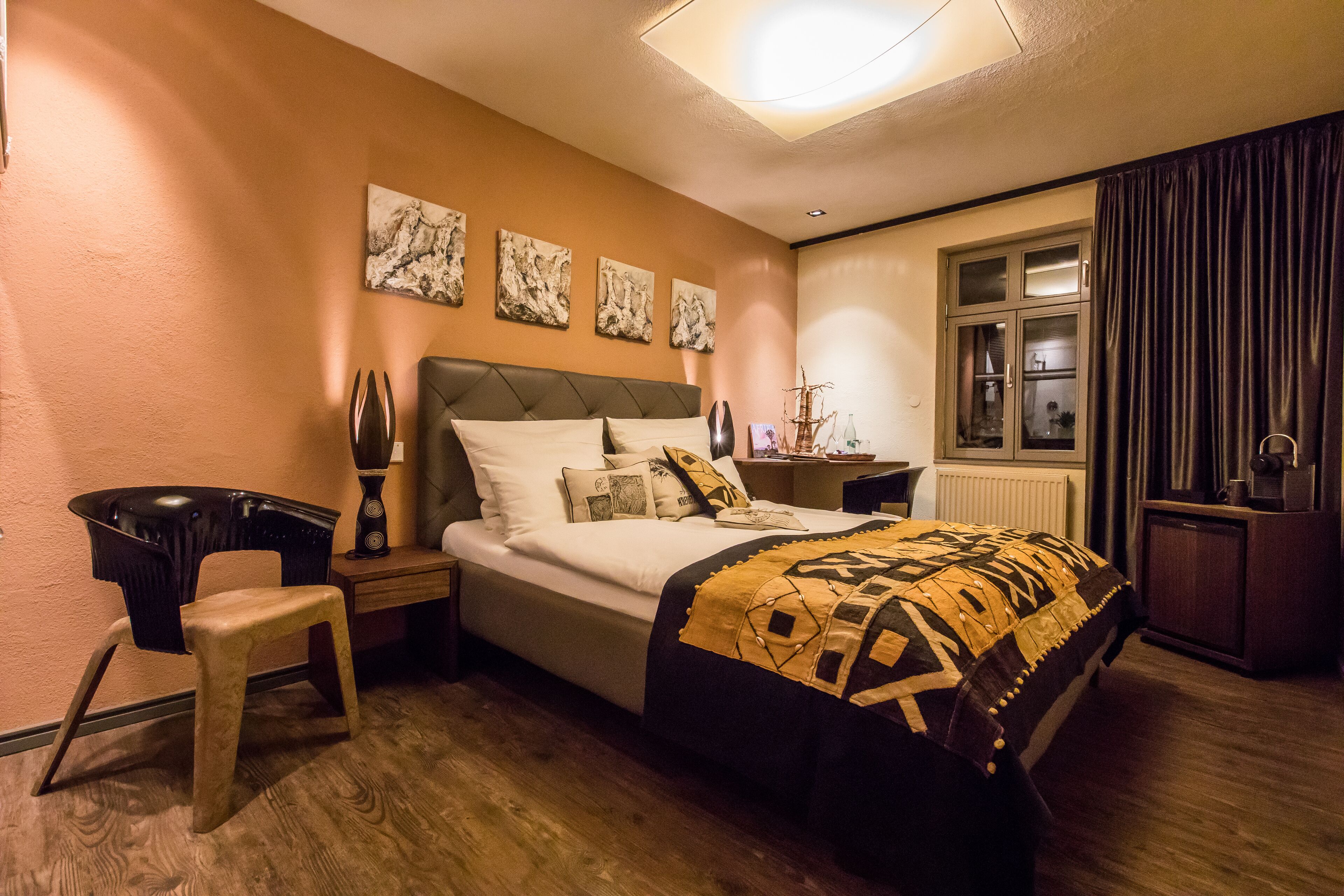 Una habitación de hotel con cama, escritorio, silla, mesita de noche y ventana con cortinas.