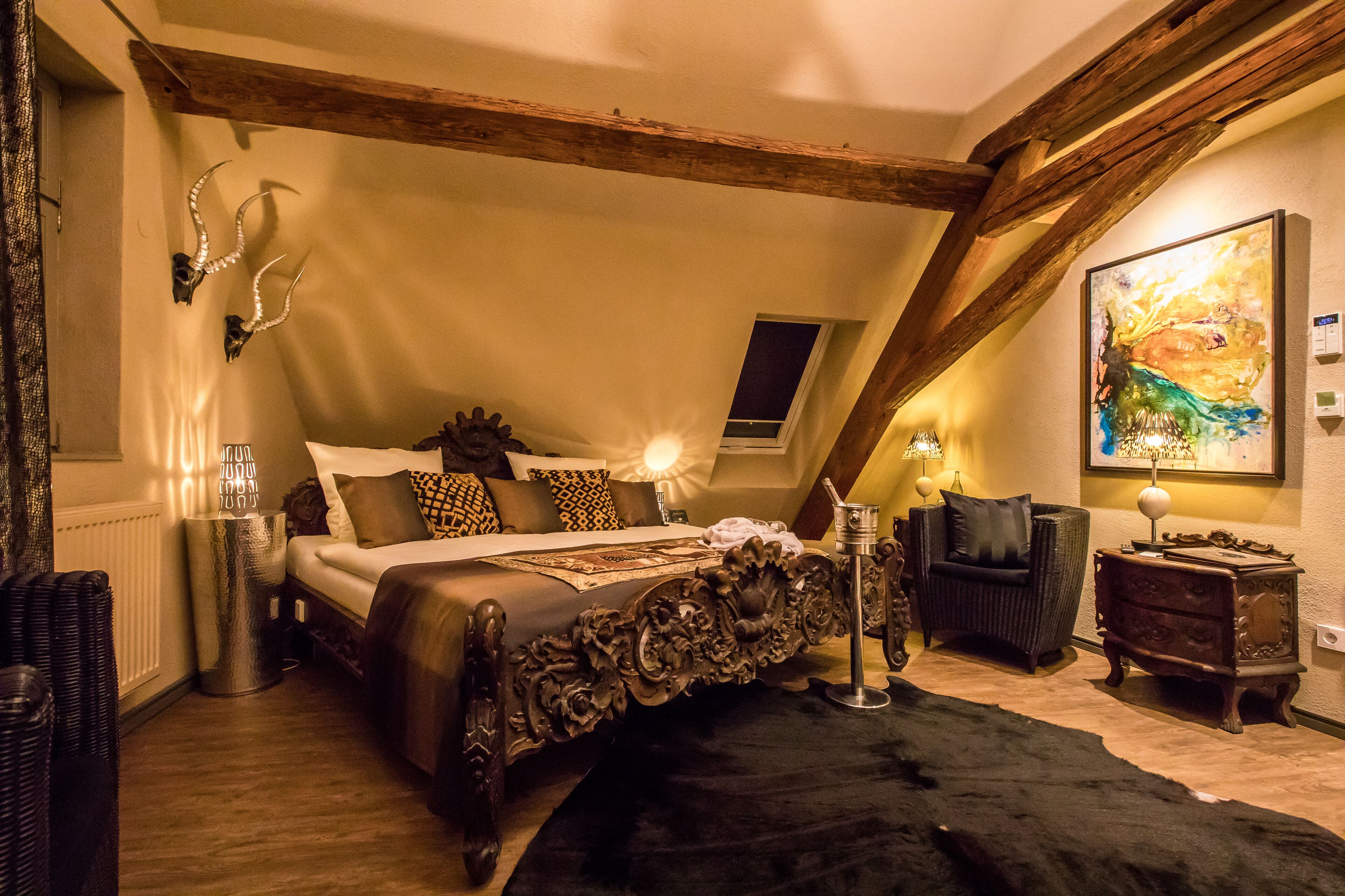 A bedroom with a large bed, wooden beams, a black rug, a dresser, and a painting on the wall.