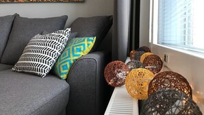 Un salon moderne avec un canapé gris, des coussins à motifs, un tableau représentant un arbre décoratif et une rangée de lampes sphériques en osier.