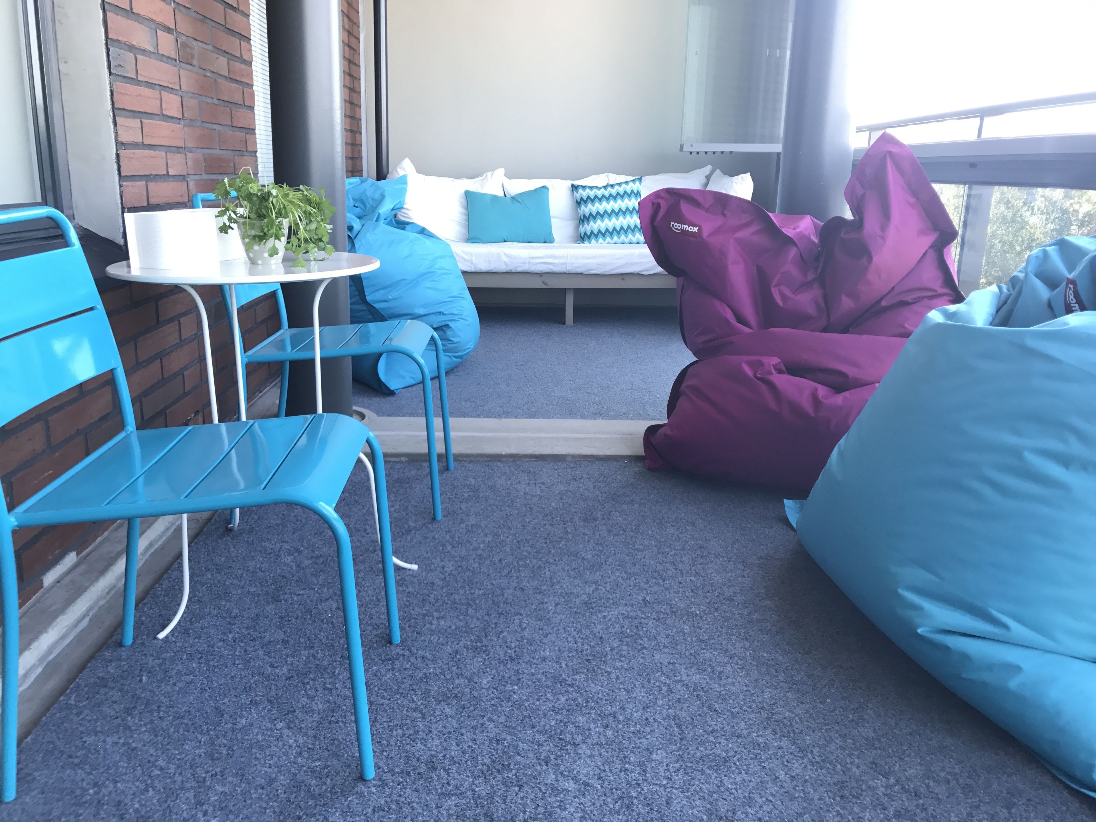 Ein gemütlicher Außenbereich mit blauen Stühlen und einem Tisch, einer gepolsterten Bank und einem Topfpflanzen.