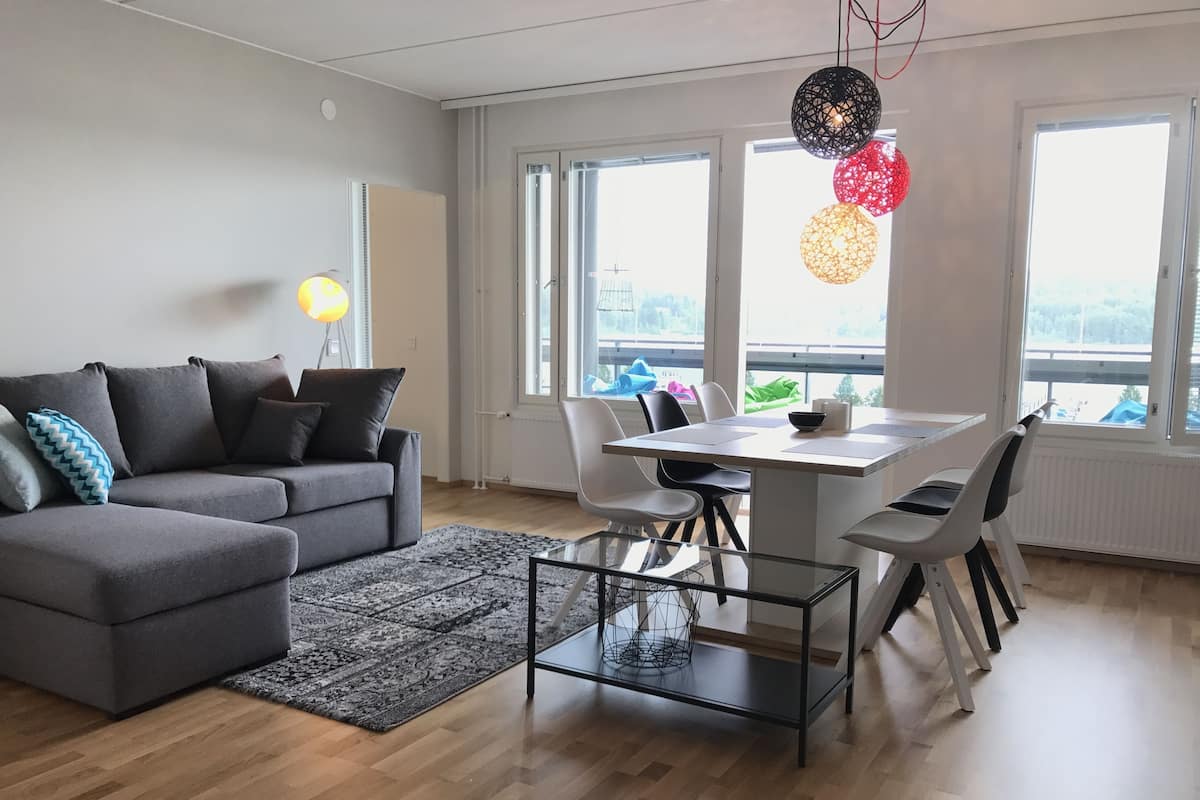 A modern living room with a grey sofa, a glass coffee table, and a dining area with a white table and chairs.