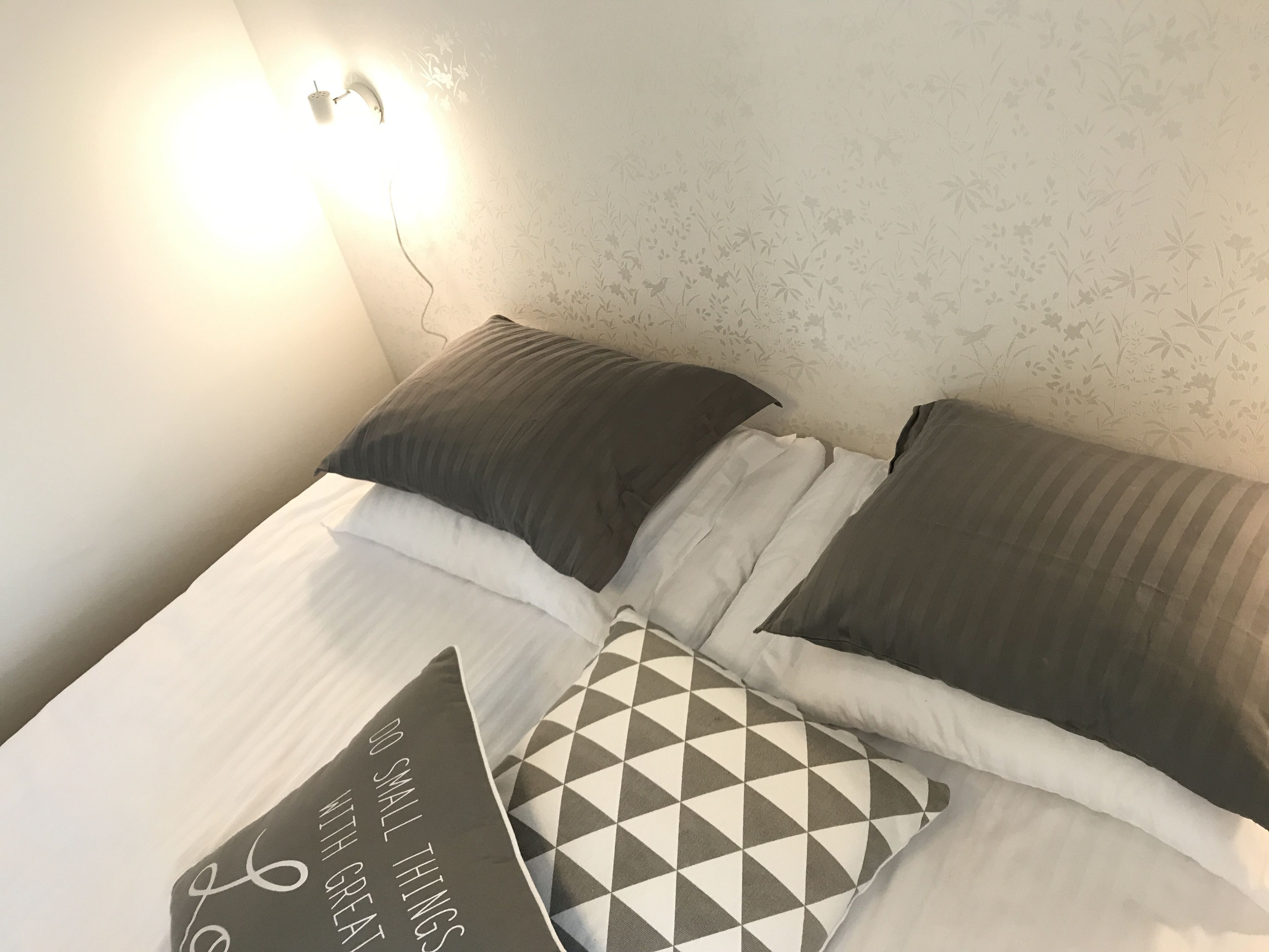 Un lit bien fait, avec du linge de lit blanc et deux oreillers : l’un orné d’un motif géométrique et l’autre d’un motif textuel.